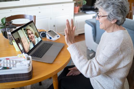 senior woman waving to doctor during a telehealth visit for a story on Matrix telehealth vs. in-home assessments